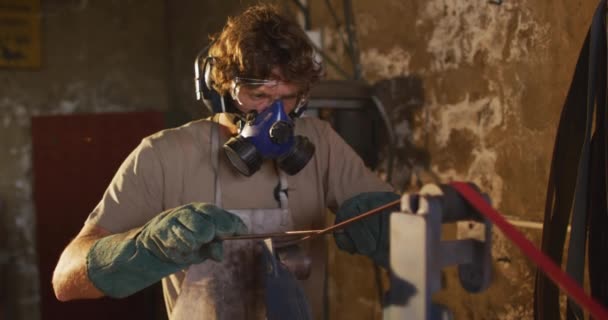 白种人男性铁匠戴着呼吸面罩 戴着护目镜 在车间里锻造金属工具 小生意和锻造铁匠的工艺 — 图库视频影像