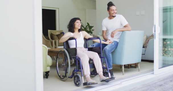 坐在轮椅上的快乐的女儿和从阳台上看到客厅的笑脸的男伴 身体残疾的福祉和家庭生活方式 — 图库视频影像