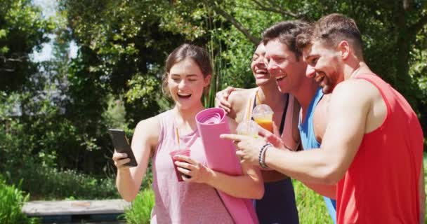 在阳光充足的公园里 一群快乐多样的男人和女人使用智能手机 在瑜伽课后聊天 室外健康 健康的爱好和积极的生活方式 — 图库视频影像
