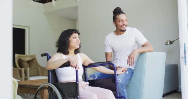 車椅子で幸せな出産の女性と笑顔の男性パートナーのリビングルームで手を握って座っている 身体障害者の健康と国内生活 — ストック動画