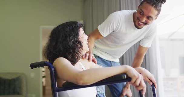 車椅子の幸せな出産女性と日当たりの良いリビングルームで受け入れる笑顔の男性パートナー 身体障害者の健康と国内生活 — ストック動画