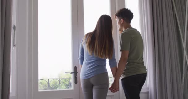 Szczęśliwa Para Dwurasowa Trzymająca Się Ręce Patrząca Przez Okno Razem — Wideo stockowe