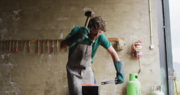 白人男性铁匠戴着安全眼镜 在车间的铁锹上锤打热金属工具 小生意和锻造铁匠的工艺 — 图库视频影像