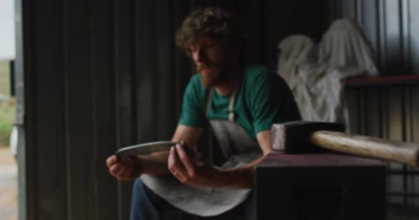 高加索男性铁匠在车间里拿着金属工具 小生意和锻造铁匠的工艺 — 图库视频影像