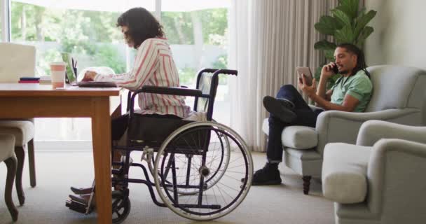 ラップトップを使って車椅子で幸せな出産の女性は 男性のパートナーのリビングルームで電話で話している 身体障害者の健康と国内生活 — ストック動画