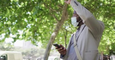 Şehirde yüzü olan, akıllı telefon kullanan ve el sallayan Afrikalı bir Amerikalı. Dijital göçebe covid 19 salgını sırasında şehirde dolanıyor..