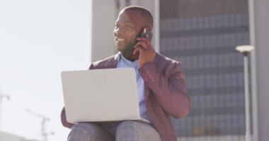 Şehirde Afro-Amerikalı bir adam merdivenlerde oturuyor, akıllı telefon ve dizüstü bilgisayar kullanıyor. Dijital göçebe şehirde geziyor, dolaşıyor..