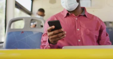 Şehirdeki Afrika kökenli Amerikalı bir adamın yüz maskesi takıp otobüste akıllı telefon kullanması. Dijital göçebe covid 19 salgını sırasında şehirde dolanıyor..