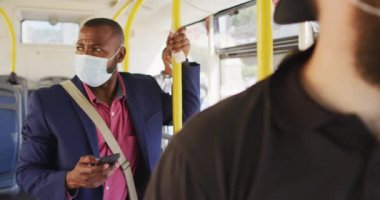 Şehirdeki Afro-Amerikan adam yüz maskesi takıyor, otobüste akıllı telefon kullanıyor. Dijital göçebe covid 19 salgını sırasında şehirde dolanıyor..