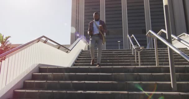 アフリカ系アメリカ人の男性が階下を歩いていて コーヒーを持っていて スマートフォンを使っている 外にも街中にもデジタル ノマドが — ストック動画
