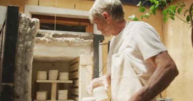 Çömlek atölyesindeki fırında önlük giymiş beyaz bir adam. yaratıcılık ve el sanatları, hobiler ve aktif emeklilik yaşam tarzı.