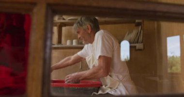Önlük giyip atölyesinde çömlekçi çarkında çömlek yapan kıdemli beyaz adam. aktif emeklilik, hobiler ve yaratıcılık.