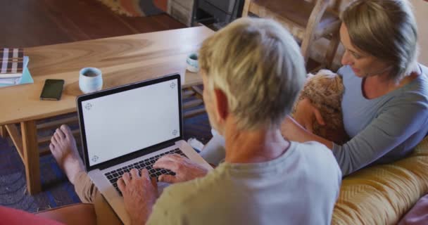 ラップトップを使用している高齢者の白人カップルを微笑み リビングルームで犬と座っています 家庭でテクノロジーを使って退職生活を送り — ストック動画