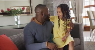 Mutlu Afro-Amerikan kızları ve babaları kanepede kucaklaşıp konuşuyorlar. Evde ailece güzel vakit geçiririz..