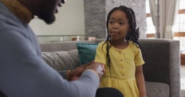 Odaklanmış Afro-Amerikan kızı kanepede oturup babasını dinliyor. Evde ailece güzel vakit geçiririz..