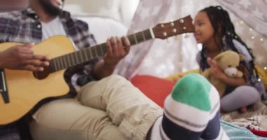 Mutlu Afro-Amerikan baba ve kızı derme çatma çadırda oturup gitar çalıyor ve şarkı söylüyor. Evde ailece güzel vakit geçiririz..