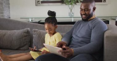 Mutlu Afro-Amerikan kızları ve babaları kanepede tablet kullanıyor. Teknolojiyle evde kaliteli bir aile zamanı..