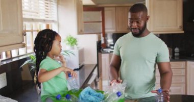 Mutlu Afro-Amerikan baba ve kızı geri dönüşüm düzenliyor ve mutfakta plastik şişeleri kırıyor. Evde ailece güzel vakit geçiririz..