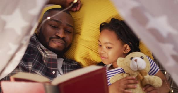 快乐的非洲裔美国父亲和女儿躺在帐篷里看书 优质家庭团聚时间 — 图库视频影像