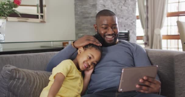 快乐的非洲裔美国女儿和父亲在沙发上使用平板电脑 与技术一起在家享受高质量的家庭生活 — 图库视频影像
