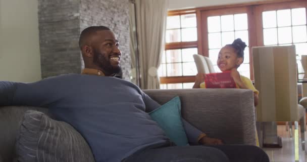 驚いた父親にプレゼントを与える幸せなアフリカ系アメリカ人の娘 家庭でのお祝いと家族での時間 — ストック動画