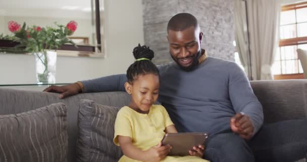 快乐的非洲裔美国女儿和父亲在沙发上使用平板电脑 与技术一起在家享受高质量的家庭生活 — 图库视频影像