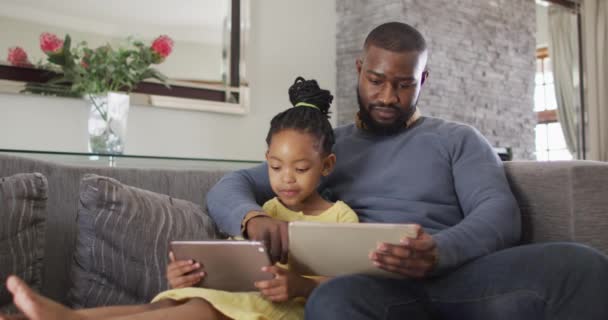 快乐的非洲裔美国人的女儿和父亲在沙发上使用平板电脑 与技术一起在家享受高质量的家庭生活 — 图库视频影像