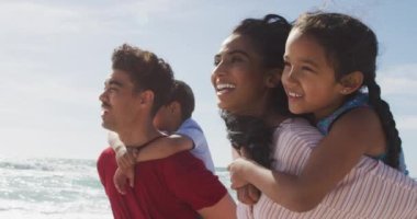 Mutlu İspanyol ebeveynler çocukları sırtında taşıyorlar ve sahilde yürüyorlar. Aile tatilleri, boş zaman ve birliktelik.