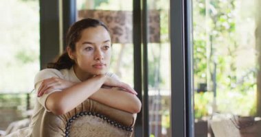 Penceredeki kanepede oturan ve dışarı bakan düşünceli melez kadın. ev hayatı ve kişisel bakım, evde boş zamanların keyfi..