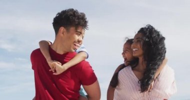 Mutlu İspanyol ebeveynler çocukları sırtında taşıyorlar ve sahilde yürüyorlar. Aile tatilleri, boş zaman ve birliktelik.