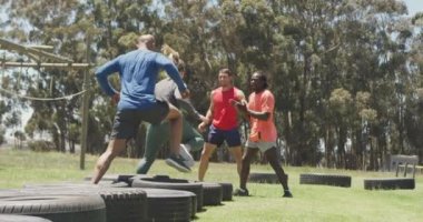 Diverse fit group running through tyres and high fiving in the sun at obstacle course. healthy active lifestyle, cross training outdoors at boot camp.