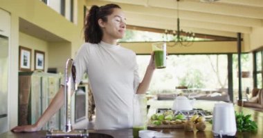 Mutfakta smoothie içen mutlu çift ırklı kadın. Sağlıklı yaşam tarzı ve evde boş vakitlerin tadını çıkarmak..