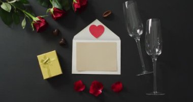 Zarfta kağıt kalp ve sevgililer gününde siyah arka planda şampanya bardakları olan güller. Sevgililer günü, aşk ve kutlama konsepti..