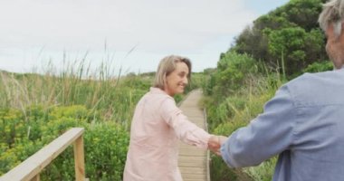 Gülümseyen Kafkasyalı çift el ele tutuşuyor ve dışarıda yürüyor. aktif emeklilik ve sağlıklı açık hava yaşam tarzı.