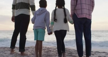 Gün batımında sahilde dikilen İspanyol ailenin arka görüntüsü. Aile tatilleri, boş zaman, birliktelik ve dışarıda zaman geçirmek..