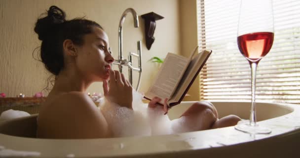 Relaxed Biracial Woman Lying Bath Foam Glass Wine Reading Book — ストック動画