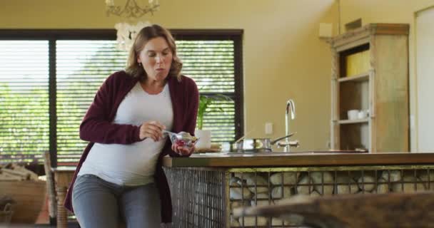 台所に座り アイスクリームを食べる白人妊婦 妊娠中や出産予定日や家で過ごす時間は — ストック動画