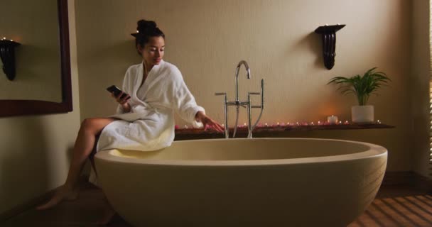 Szczęśliwa Birasowa Kobieta Siedząca Szlafroku Wannie Przygotowująca Kąpiel Korzystająca Smartfona — Wideo stockowe