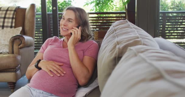Ευτυχισμένη Καυκάσια Έγκυος Γυναίκα Κάθεται Στον Καναπέ Και Έχει Τηλεφώνημα — Αρχείο Βίντεο