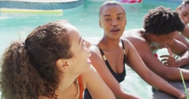 İçkileri yüzme havuzunda gülen iki farklı bayan arkadaş. Havuz partisinde arkadaşlarıyla takılıyor..