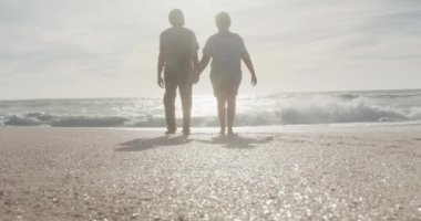 Latin hispanic couple holding hands, walking on beach at sunset. love, romance and active retirement lifestyle.