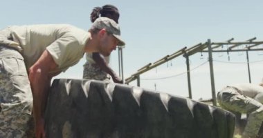 Güneşte ordunun engelli parkurunda traktör lastikleri takla atan bir grup asker. Sağlıklı aktif yaşam tarzı, acemi birliğinde çapraz eğitim..