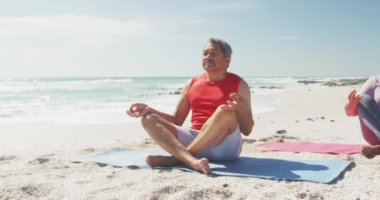 Plajdaki minderlerde yoga yapan rahat İspanyol kıdemli çift. Sportif, sağlıklı ve aktif emeklilik yaşam tarzı.