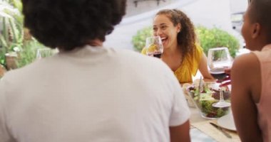 Bir grup erkek ve kadın arkadaş terasta yemek yiyor, gülüyor ve şarap içiyor. Evde ve bahçede arkadaşlarla takılıyorum..