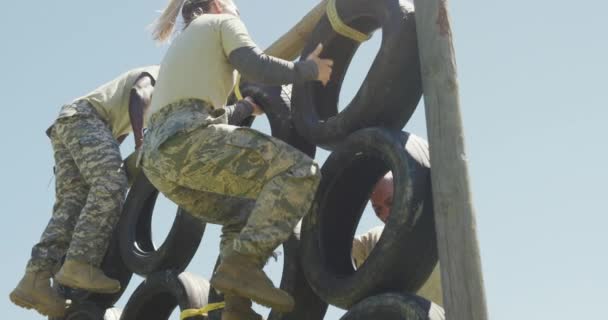 太陽の下で軍の障害物コース上の均一なクライミングタイヤの壁と戦う多様なグループの男性兵士 健康的なアクティブライフスタイルブートキャンプで屋外でのクロストレーニング — ストック動画