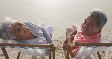 Mutlu İspanyol çift gün batımında plajda güneşleniyorlar ve kameraya bakıyorlar. Aşk, romantizm ve aktif emeklilik yaşam tarzı.