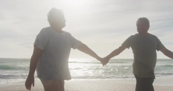 幸せなヒスパニック系のシニアカップルの手を握って ビーチで日没時に歩いてください 愛ロマンス活動的な退職生活 — ストック動画