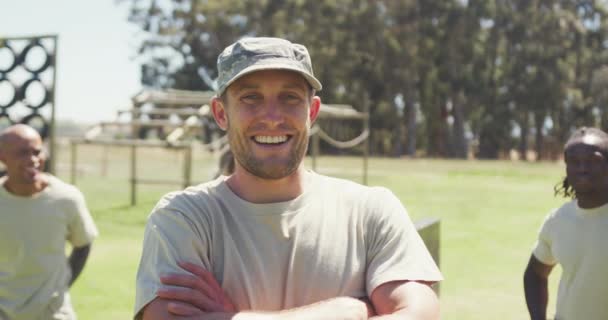 一个头戴军帽的高加索男兵的画像 在障碍面前微笑着 身后有许多不同的人群 健康积极的生活方式 在新兵训练营的室外交叉训练 — 图库视频影像