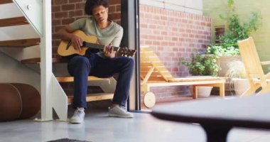 Mutlu Afrikalı Amerikalı adam gitar çalıyor ve evde şarkı söylüyor. Boş zaman, evde tek başına dinlenmek..