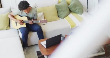 Afrikalı Amerikalı adam evde dizüstü bilgisayar kullanarak gitar çalıp şarkı söylüyor. Teknoloji kullanarak boş zaman geçirmek, evde tek başına dinlenmek..